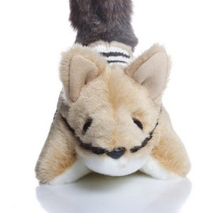 May include: A plush toy animal with brown fur on its tail and a striped white and black sweater. The animal has a light brown body with a white face and black eyes.