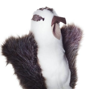 May include: A white and brown plush bird puppet with a long brown stick attached to the bottom. The bird has a long beak and a fluffy body.