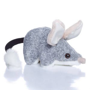 May include: A gray and white plush toy resembling a bandicoot with large ears and a long tail. The toy has a realistic appearance with a soft, furry texture.