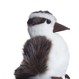 May include: A white and brown plush toy bird with a black eye. The bird is sitting on a white surface.