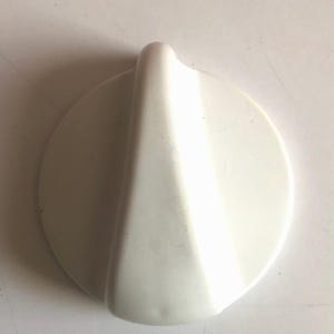 Puede incluir: Pomo de plástico blanco con forma redondeada y puntiaguda. El pomo está diseñado para su uso con electrodomésticos.