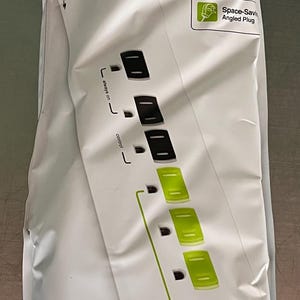 Può includere: Una ciabatta elettrica TrickleStar a 7 prese bianca nella sua confezione originale. La confezione presenta testo verde e nero, un cavo di alimentazione robusto da 3 piedi e dettagli sulla protezione da sovratensione. Prese nere e verdi.