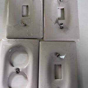 May include: Four off-white electrical wall plates. Two have single switch openings, one has a double outlet, and the last has a single switch opening. Each plate is secured with screws and tape.