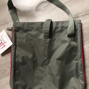 May include: A green canvas tote bag with red trim and a long adjustable strap. The bag has a zipper closure and a small pocket on the front. The bag is labeled "free gift" with the Calvin Klein logo.