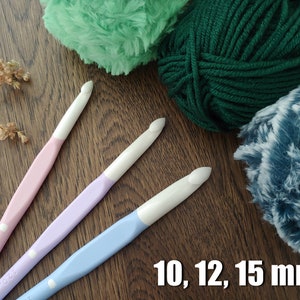 May include: Three crochet hooks with white heads and pastel pink, lavender, and light blue handles, accompanied by three balls of yarn in green, dark green, and blue-white variegated textures, with the text 10, 12, 15 mm visible.