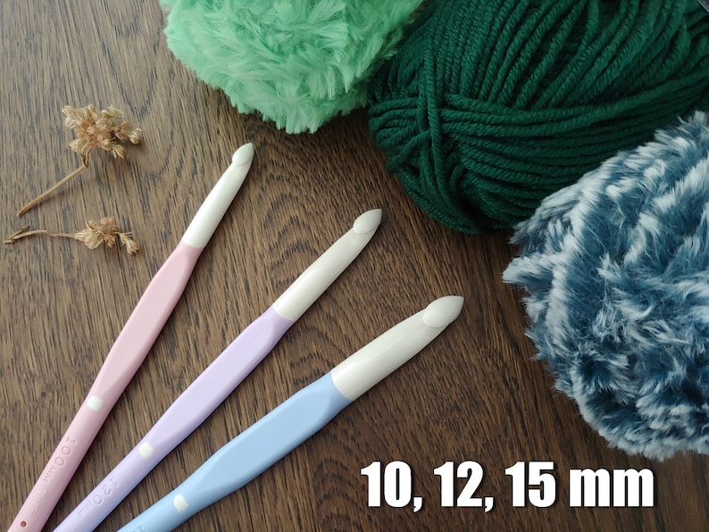 May include: Three crochet hooks with white heads and pastel pink, lavender, and light blue handles, accompanied by three balls of yarn in green, dark green, and blue-white variegated textures, with the text 10, 12, 15 mm visible.