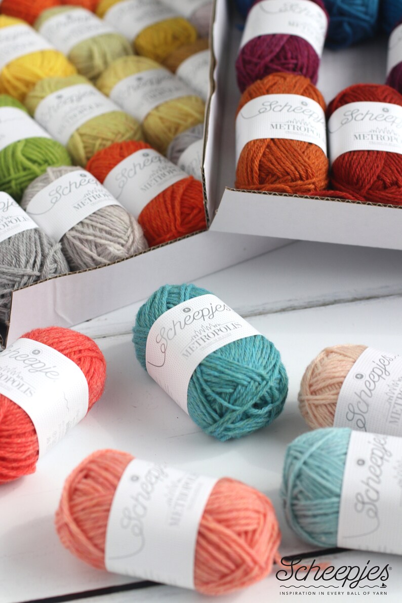 May include: A variety of colorful yarn balls in different shades of orange, red, green, blue, and pink. The yarn is labeled "Scheepjes Metropolis" and "Scheepjes".