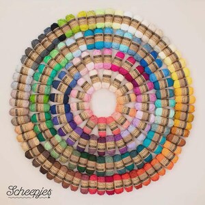 May include: A circular arrangement of colorful yarn skeins, showcasing a spectrum of hues from light pastels to deep shades. Each skein is wrapped with a brown paper label. The image features the "Scheepjes" logo in the bottom left corner.