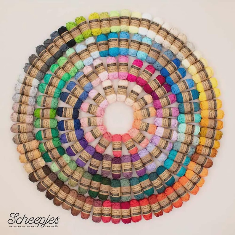 May include: A circular arrangement of colorful yarn skeins, showcasing a spectrum of hues from light pastels to deep shades. Each skein is wrapped with a brown paper label. The image features the "Scheepjes" logo in the bottom left corner.