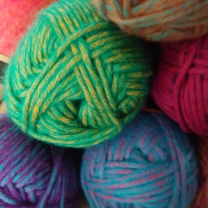 May include: A collection of yarn balls in various colors including bright green with yellow flecks, deep purple, magenta, teal with pink flecks, and brown. A partial paper label with the text 'pjes' and 'XL' is visible on the left side.