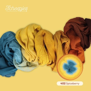 Peut inclure: Une pelote de laine Scheepjes étiquetée 402 Spiceberry, présentant un dégradé allant du bleu au jaune, à l'orange et au marron. Le fil est présenté sous forme de pelote circulaire à côté d'échantillons de tricot drapés aux couleurs allant du bleu au jaune, à l'orange et au brun foncé.