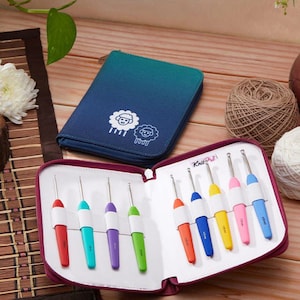 Può includere: Una custodia con cerniera color bordeaux con un interno bianco contiene un set di otto uncinetti colorati. La custodia ha il testo "KnitPro" stampato sul davanti. La custodia è aperta e gli uncinetti sono visibili.