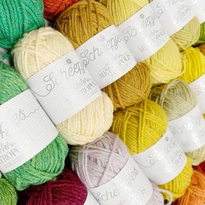 Pu&ograve; includere: Primo piano di una variet&agrave; di gomitoli di filato in diversi colori, tra cui verde, giallo, arancione e crema. Il filato &egrave; etichettato "Scheepjes" e "Metropolis".