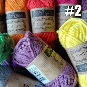 May include: Close-up of colorful yarn skeins. The image features various shades of yarn, including orange, red, purple, and yellow. Each skein has a label that reads "Scheepjes Cahlista". The number "#2" is visible on one of the labels. Ideal for knitting and crochet projects.