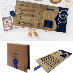 Può includere: Un set di ferri da maglia Pony Perfect con custodia pieghevole in finta pelle scamosciata marrone e chiusura blu. Il set include diverse coppie di ferri in legno con punte metalliche, cavi circolari trasparenti, segnapunti dorati e rocchetti in legno.