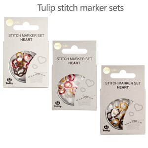 May include: Three packs of Tulip brand stitch markers shaped like hearts. Each pack features a different colour combination of red, white, gold, and brown.
