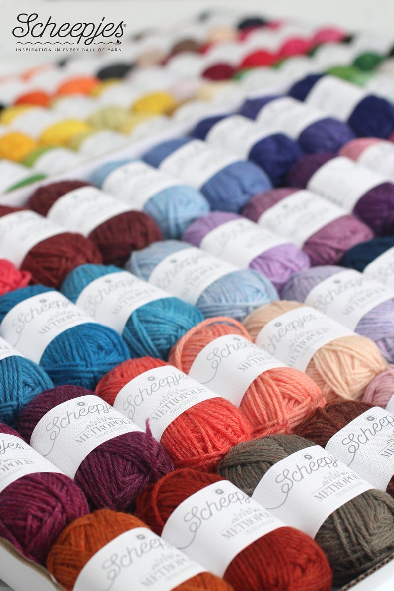 May include: A close-up view of a variety of colorful yarn balls, each labeled with the brand name "Scheepjes" and the yarn type "Metropolis".