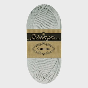 May include: A skein of light gray yarn with a brown label. The label features the brand name "Scheepjes" in cursive and the word "Catona" in a decorative frame. The yarn is tightly wound.
