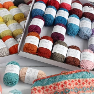 May include: A variety of colorful yarn skeins in different shades of red, orange, yellow, green, blue, purple, brown, and pink. The yarn is arranged in two boxes and on a white surface. The yarn is labeled "Scheepjes" and "Wool".