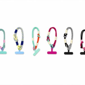 May include: Six phone lanyards in a row, each with a looped rope design and a T-shaped base. The lanyards are in various colours, including teal, pink, grey, and black, with accents of yellow, orange, and purple. The lanyards are for mobile phones.