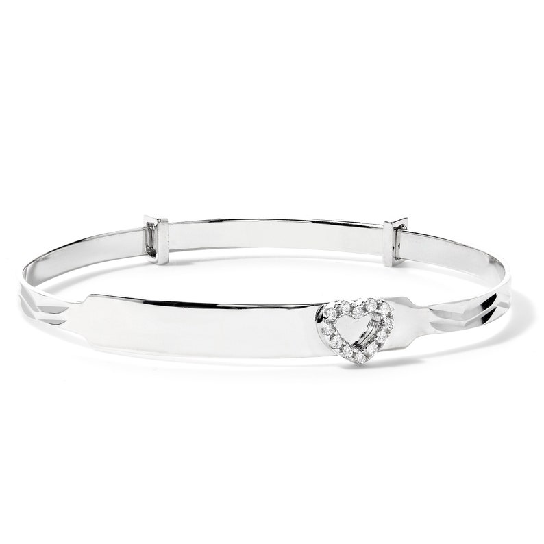 May include: A silver-toned bangle bracelet with a heart-shaped charm. The heart is encrusted with small, clear gemstones. The bracelet has an adjustable clasp and a smooth, polished finish. The design is simple and elegant.
