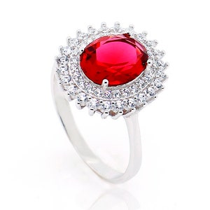 以下が含まれることがあります： 大きな赤い楕円形の宝石が、小さな白い宝石の二重の列で囲まれた銀の指輪です。