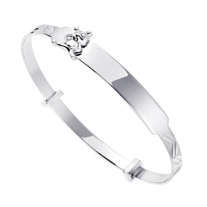 May include: A polished silver-tone bangle bracelet featuring a smooth, flat identification plate section and a small, raised bear-shaped charm with a single clear stone accent. The band includes adjustable sliding components and textured detailing.