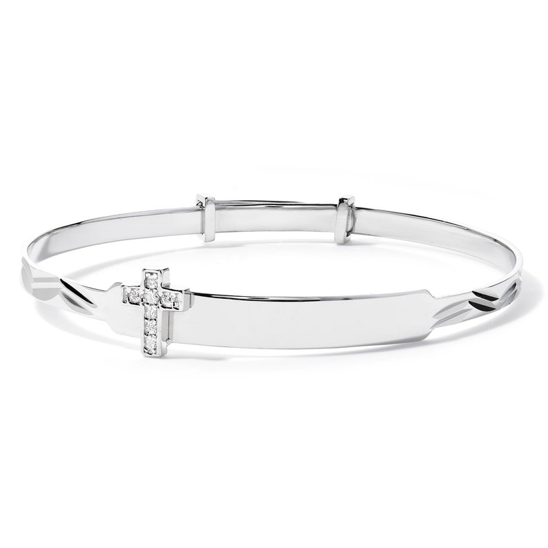 May include: A silver-toned adjustable bangle bracelet. The bracelet features a rectangular nameplate and a cross charm adorned with small, clear gemstones. The design is simple and elegant, suitable for a religious occasion.