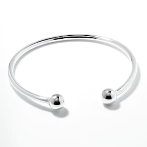May include: A silver bangle bracelet with two round ball accents at the ends.