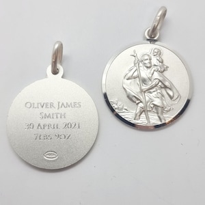 Puede incluir: Colgante de plata con una imagen de San Cristóbal en un lado y una inscripción personalizada en el otro. La inscripción dice "Oliver James Smith, 30 de abril de 2021, 7 lbs 9 oz".