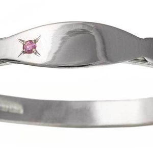 May include: A silver baby bangle with an engraved floral design and a pink gemstone set in the centre.