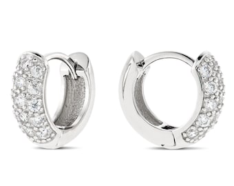 May include: A pair of silver hoop earrings. Each earring features a row of small, clear gemstones along the outer curve. The earrings are shown against a white background, highlighting their polished, reflective surface.