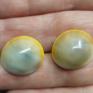 May include: Two round, polished cabochons with a yellow and white colour gradient. The cabochons have a glossy finish and a slightly domed shape. They are likely used for jewellery making or other craft projects.