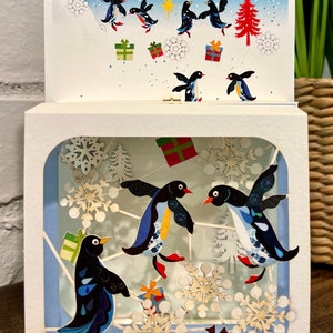 RBX811 Tarjeta navideña cortada con láser con pingüinos en la nieve en caja mágica