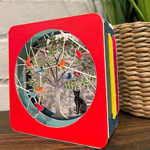 Tarjeta desplegable 3D cortada con láser con un gato negro bajo un árbol con pájaros salvajes