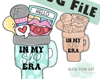Pode incluir: Uma caneca azul turquesa com uma alça branca e uma borda branca. A caneca tem um design preto e branco que diz "In My SLP Era". A caneca está cheia de um microfone, uma paleta de maquiagem, uma lâmpada, um coração e um par de lábios.