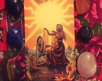 Puede incluir: Una carta de tarot con un fondo amarillo y una mujer haciendo girar una rueda. La carta está etiquetada como "19 - Sol".