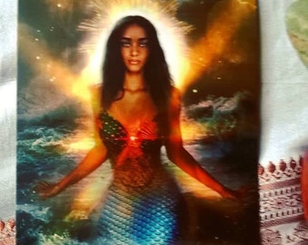 Puede incluir: Yemoja, la Diosa de Todo lo que Fluye, se representa como una sirena con una cola azul y verde, rodeada de un halo brillante. El texto dice "Soy un océano de energía creativa. Doy a luz a lo que existe dentro de mí."