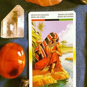 Puede incluir: Carta de tarot de la Reina de Copas con una mujer vestida con una t&uacute;nica roja y negra sosteniendo una copa dorada. La carta tiene el texto "Queen of Chalices, Reina de Copas, Regina di Coppe, Reine de Coupes, K&ouml;nigin der Kelche, Bekers Koningin" en varios idiomas.