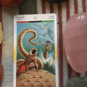 Puede incluir: Carta de tarot que representa el Nueve de Copas, tambi&eacute;n conocido como el Nueve de Copas. La carta muestra a un hombre con un tocado de pie cerca de una serpiente, una mujer en el agua y nueve copas doradas en el suelo. La carta est&aacute; titulada "Chalices, Copas, Kelche, Bekers, Coppe, Coupes".