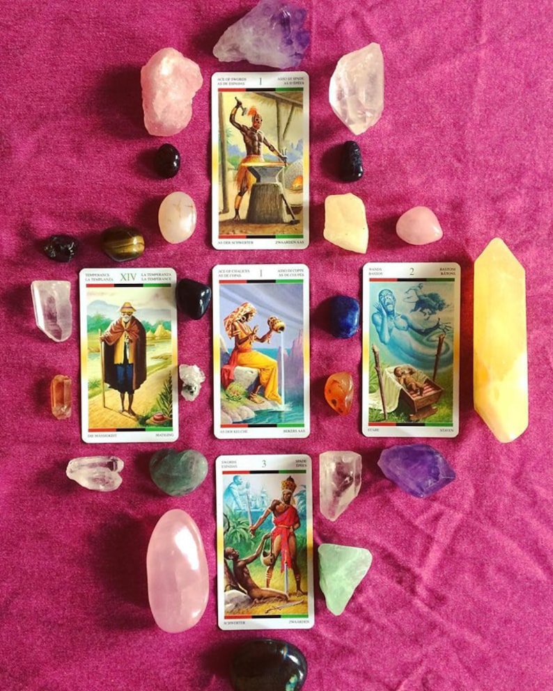 Puede incluir: Un despliegue de cartas de tarot con varios cristales sobre un fondo de tela rosa. Las cartas son de la baraja "Tarot of the Divine" e incluyen las cartas "As de Espadas", "XIV Templanza", "I Copas", "II Espadas" y "III Varitas".