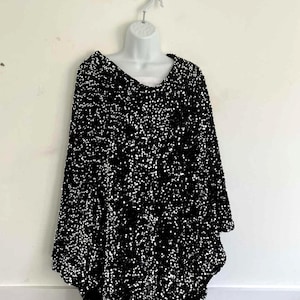 May include: Black sequin poncho with a scoop neckline, displayed on a white mannequin. The poncho has a loose, asymmetrical hemline and is covered in small, reflective sequins. A stylish, eye-catching garment.