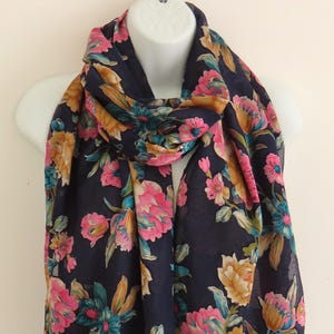 May include: A navy blue floral scarf with pink, yellow, and green flowers. The scarf is made of a lightweight fabric and is perfect for adding a touch of color to any outfit.