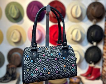 May include: A black leather handbag with a geometric pattern in white, blue, green, yellow, and red. The bag has a top handle and a zipper closure.