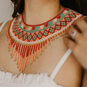 May include: A colorful beaded necklace with a geometric pattern and fringe. The necklace is made of red, orange, white, green, and blue beads.