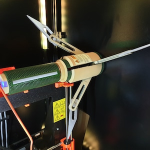 May include: A 3D printer component with a green mesh cylinder, beige cylindrical sections, and silver support arms. The device is mounted on an orange and black 3D printer frame, with a blue light visible.