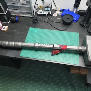 May include: A silver-colored hammer with a textured head and a long handle. The handle is wrapped in a red and black plaid fabric.