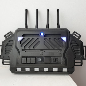 Puede incluir: Un dispositivo negro con cuatro antenas y una luz azul. El dispositivo tiene una serie de botones y un interruptor en la parte delantera.