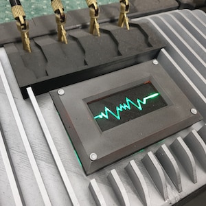 May include: A close-up of a gray metal panel with a green and red digital display showing a heart rate. The display is surrounded by a black frame with silver screws.