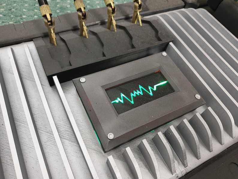 May include: A close-up of a gray metal panel with a green and red digital display showing a heart rate. The display is surrounded by a black frame with silver screws.